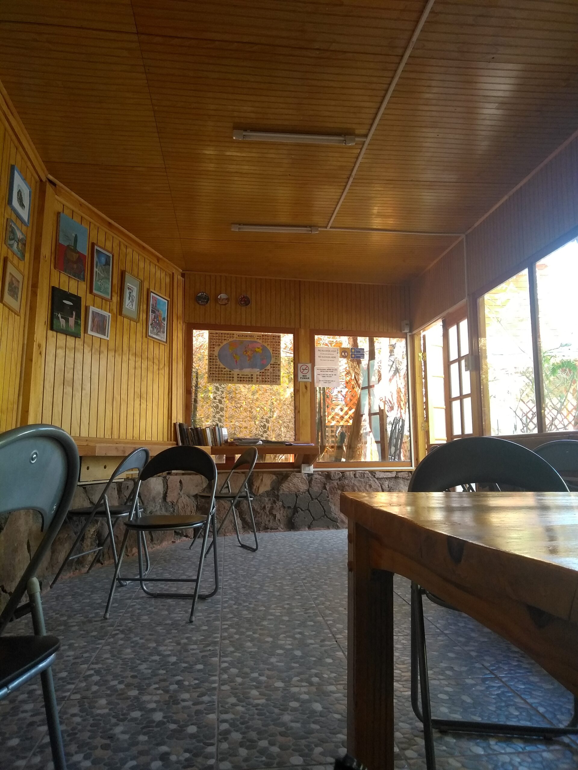 Sala de uso comum do Hostal Sonchek, com mesas, cadeiras e paredes de madeira