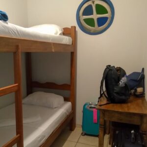 Beliche com duas camas, janelinha redonda e escrivaninha de apoio no quarto da hospedagem