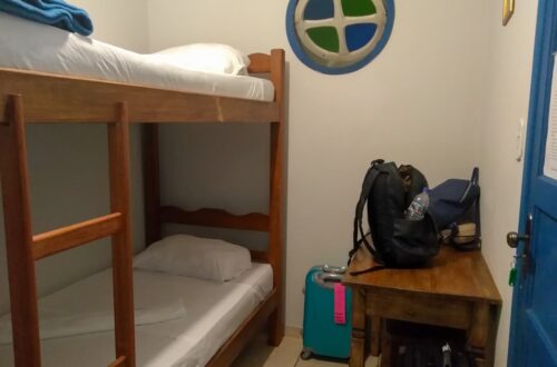 Beliche com duas camas, janelinha redonda e escrivaninha de apoio no quarto da hospedagem