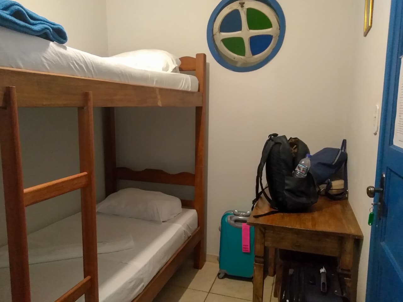 Beliche com duas camas, janelinha redonda e escrivaninha de apoio no quarto da hospedagem