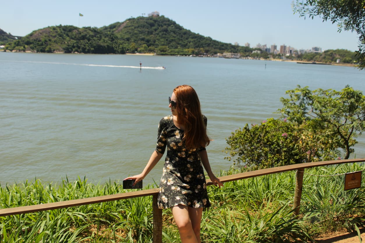 Mulher ao centro na Praia do Suá, na Praça do Papa em Vitória, com a Baía de Vitória ao fundo, assim como a cidade de Vila Velha