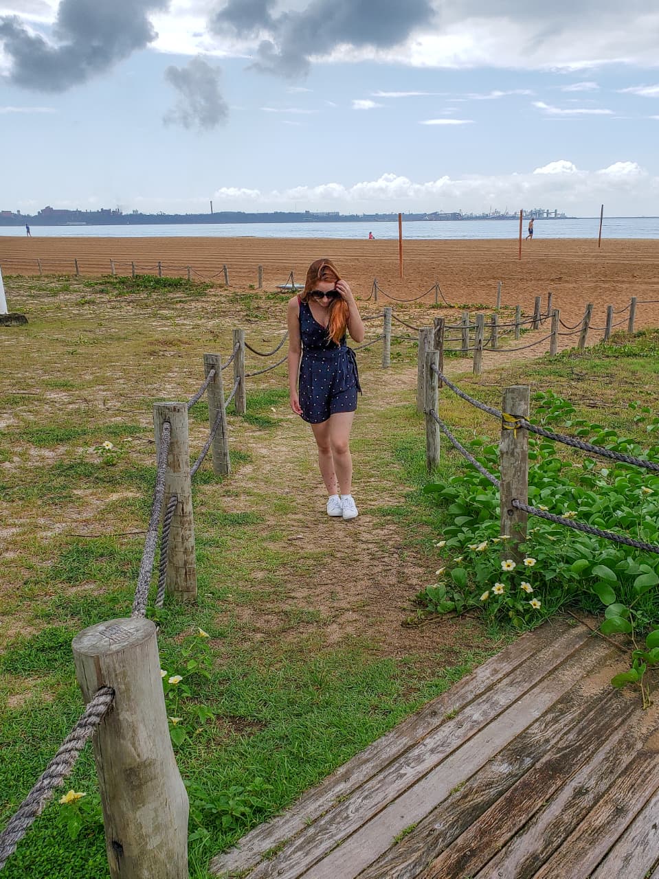 Mulher andando em trilha na orla de Mata da Praia com mar e céu com nuvens ao fundo