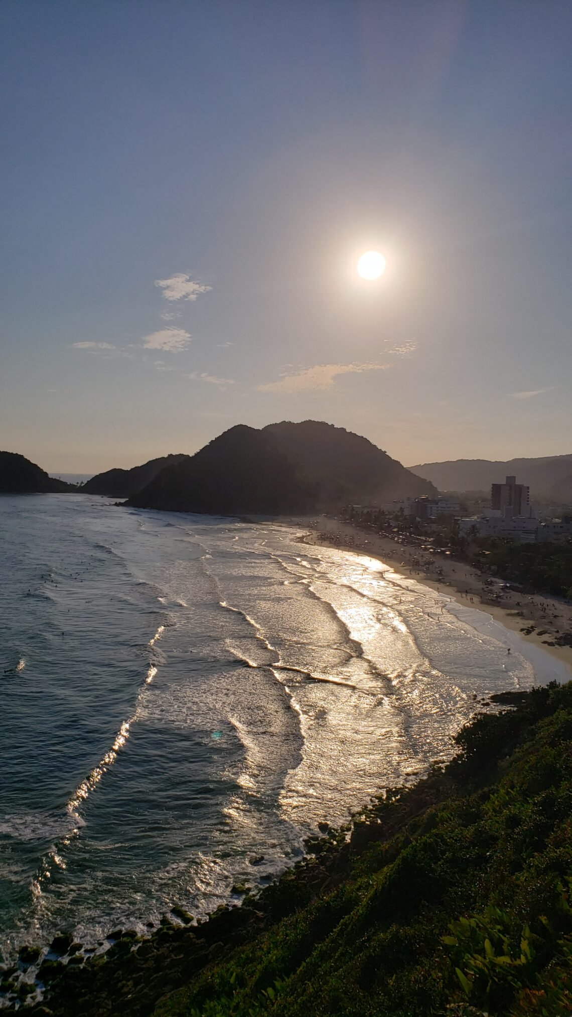 Pôr do Sol no Mirante das Galhetas, no Guarujá. Montanhas emolduram a orla ao fundo, com o mar tomando boa parte da foto