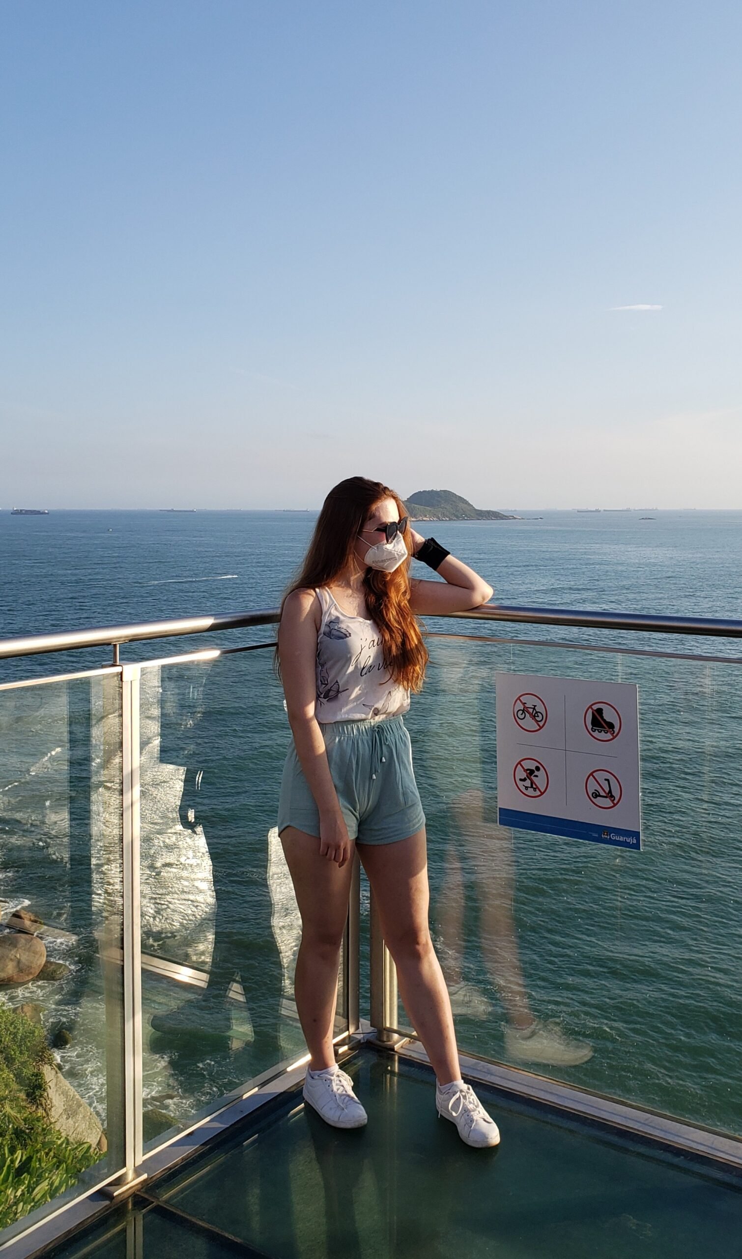 Mulher no centro da parte de vidro do Mirante das Galhetas, com o céu e o mar ao fundo