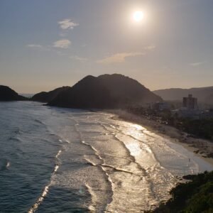 Pôr do Sol no Mirante das Galhetas, no Guarujá. Montanhas emolduram a orla ao fundo, com o mar tomando boa parte da foto